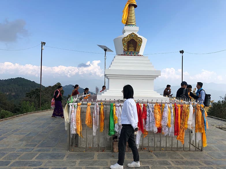 A white stupa on a hilltop in Nepal with mountains in the background