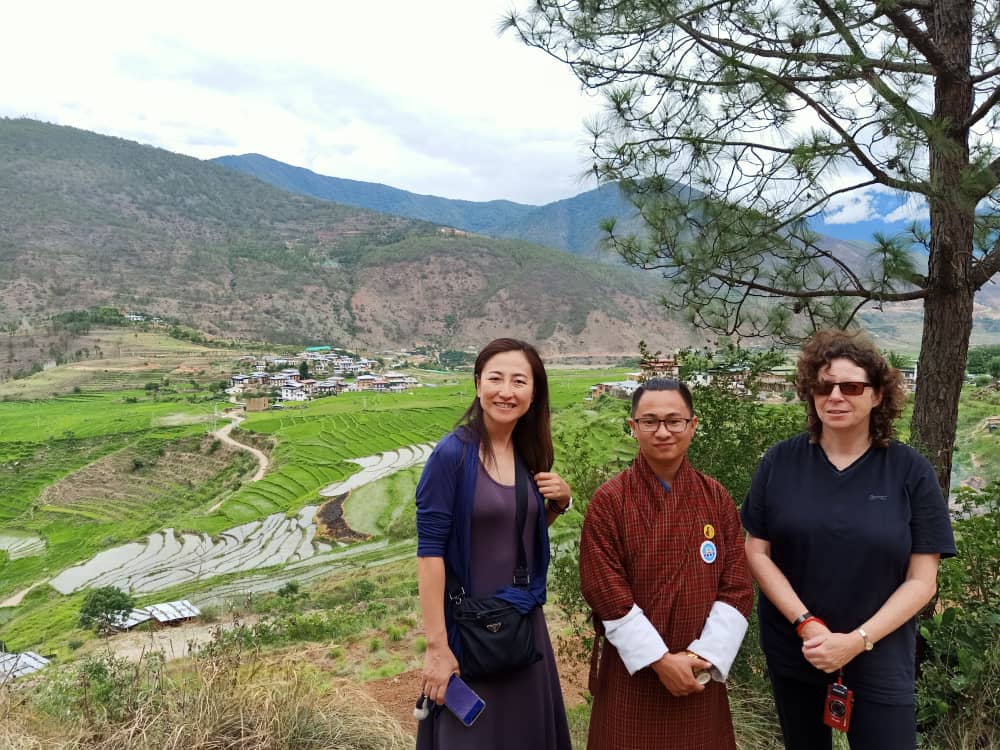 Three people on a hill overlooking a village and rice paddies in Bhutan